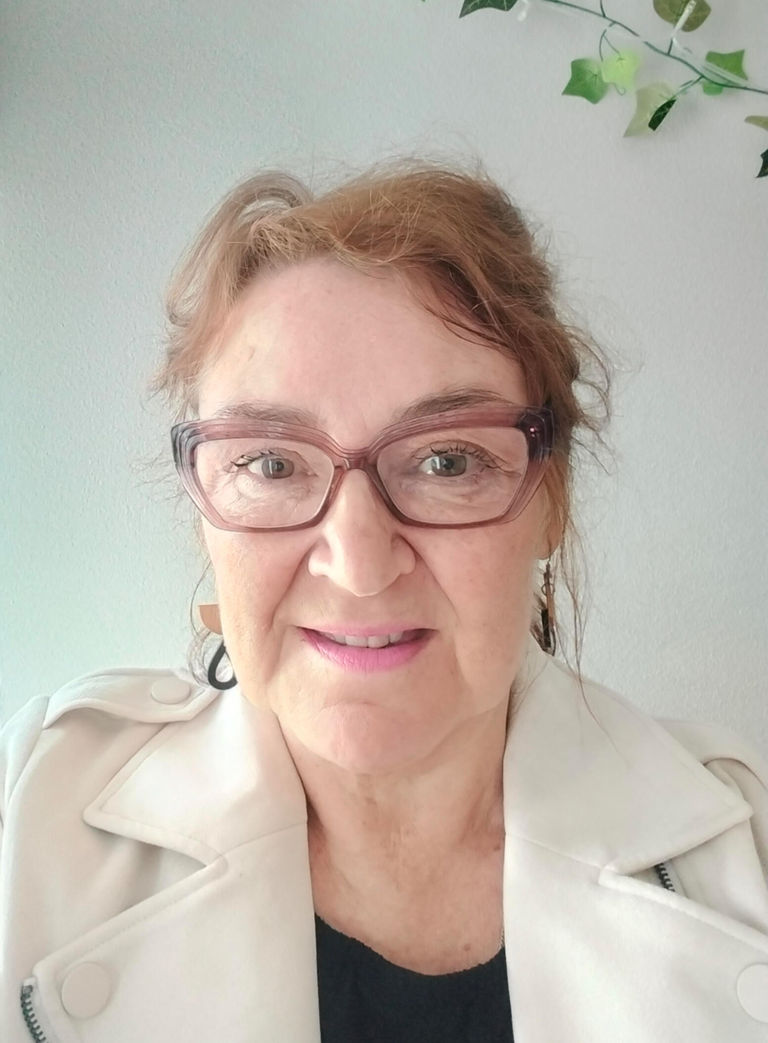 Hymyilevä nainen katsoo kameraan. Hänellä on silmälasit, hiukset kiinni ja huulipunaa.